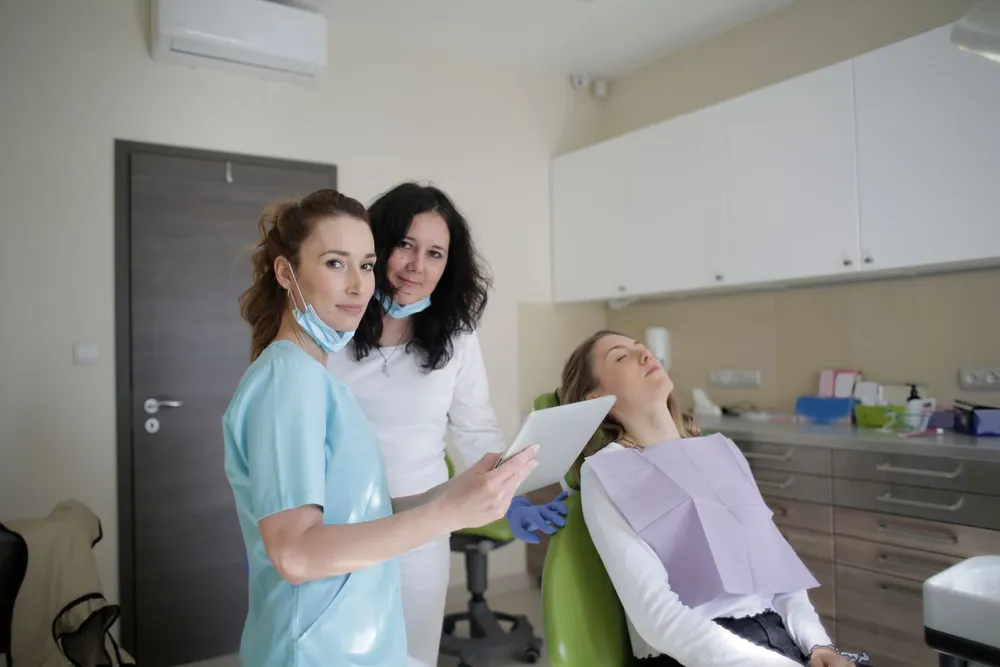 Auxiliar e dentista em um consultório odontológico, com uma paciente deitada na cadeira ao fundo