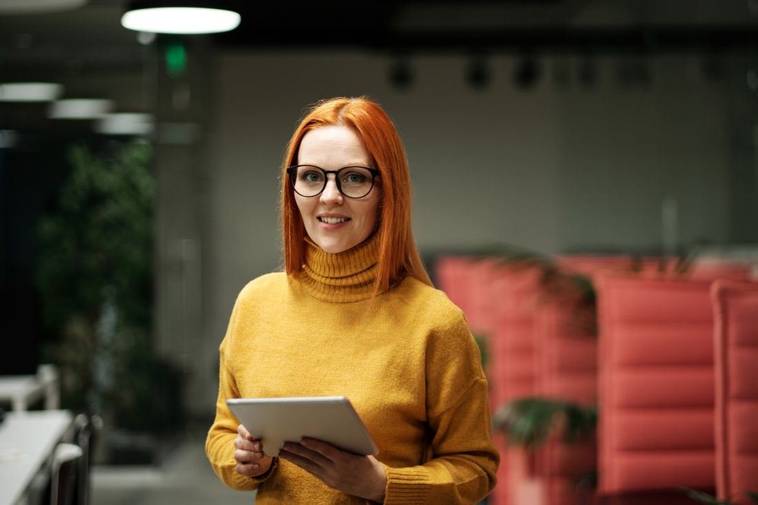 Mulher sorrindo, segurando um tablet em um escritório moderno